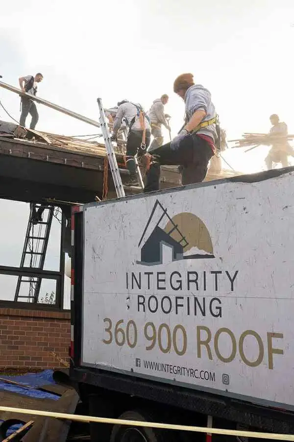 Staff on a roof working the project with an Integrity Roofing and Construction sign below.